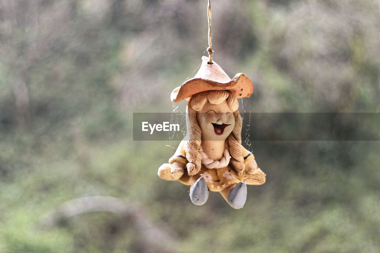 CLOSE-UP OF FIGURINE TOY HANGING FROM TREE