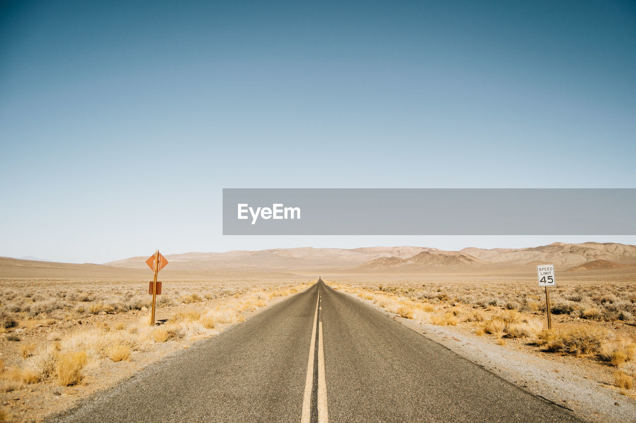 Empty straight road with traffic signs in desert of usa on sunny day