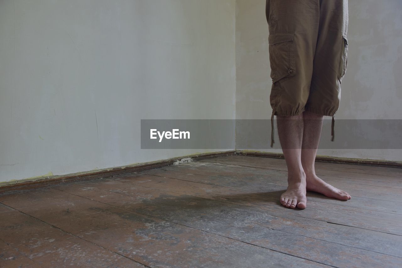 Low section of man standing on hardwood floor at home