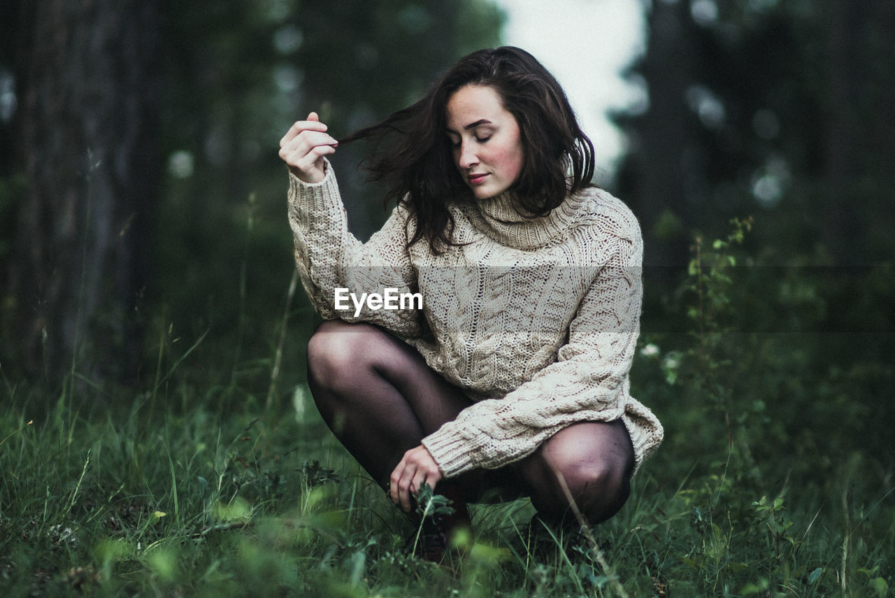 Young woman sitting on grass against trees