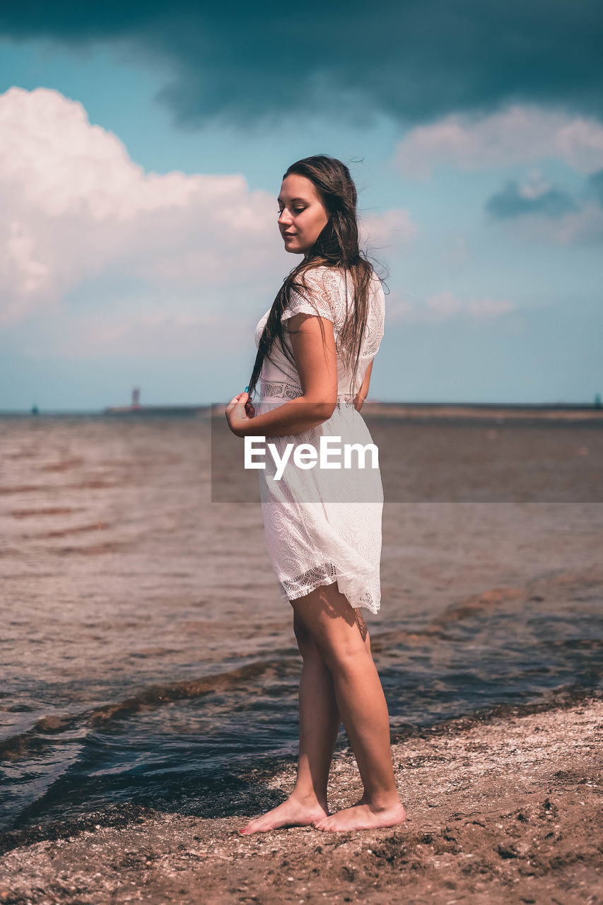 YOUNG WOMAN STANDING ON BEACH