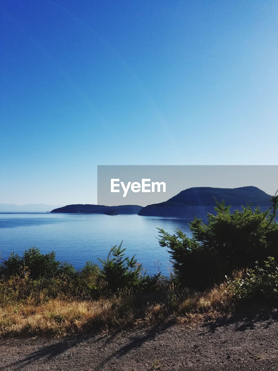 SCENIC VIEW OF SEA BY MOUNTAINS AGAINST CLEAR BLUE SKY