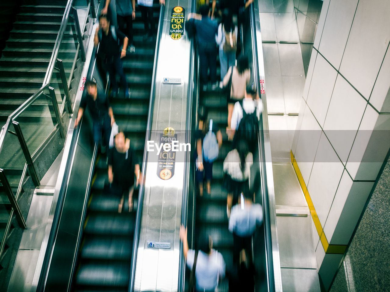 REAR VIEW OF WOMAN ON ESCALATOR AT RAILROAD STATION PLATFORM