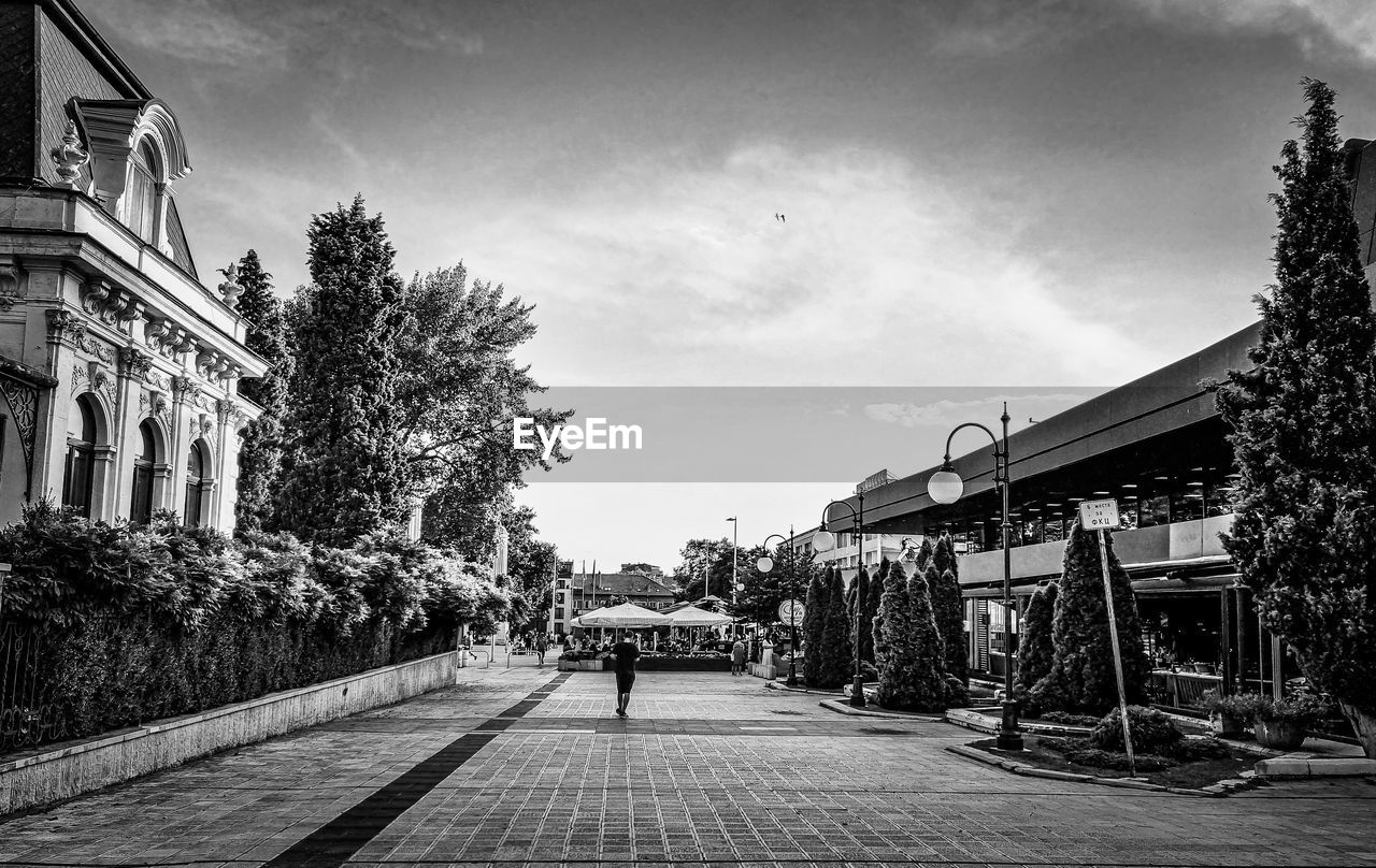 PEOPLE ON FOOTPATH BY BUILDINGS IN CITY AGAINST SKY