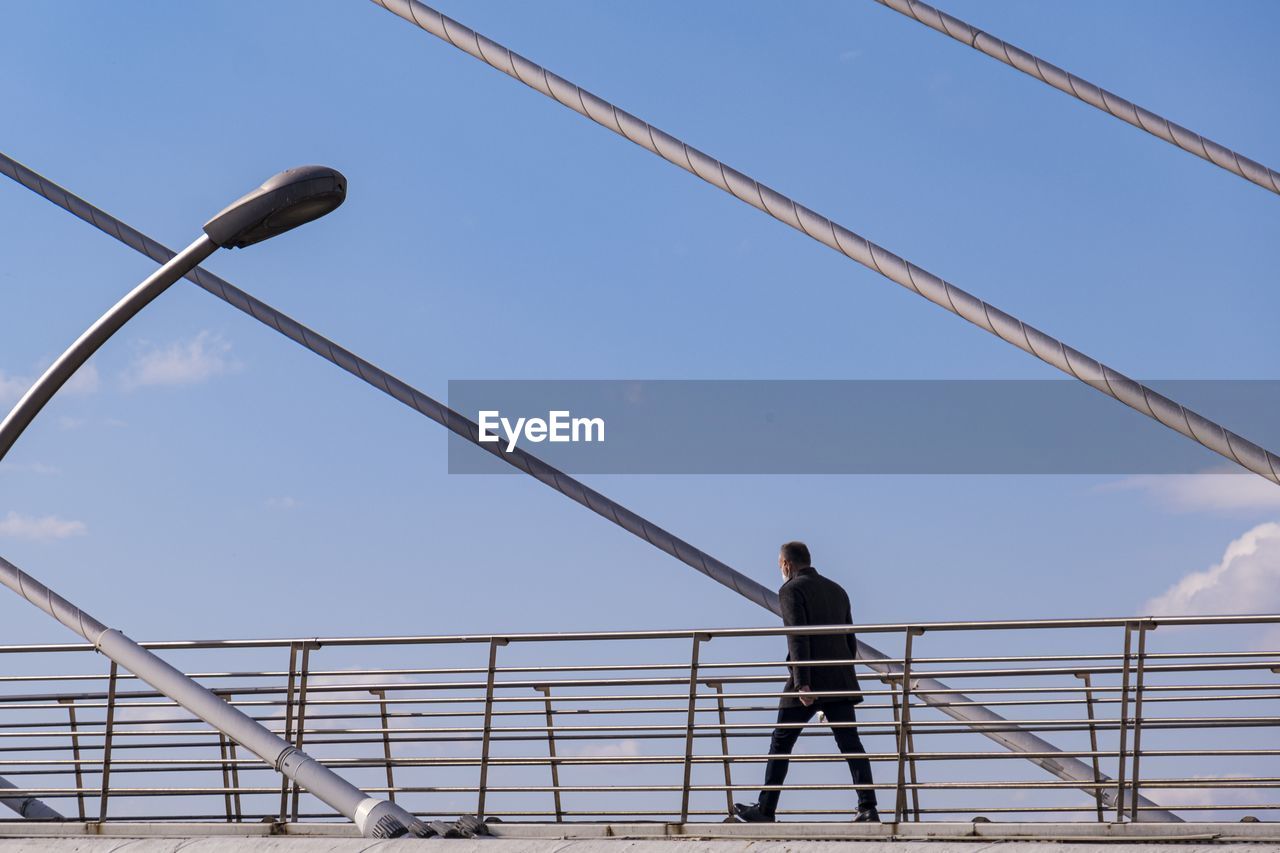 LOW ANGLE VIEW OF MAN STANDING ON RAILING