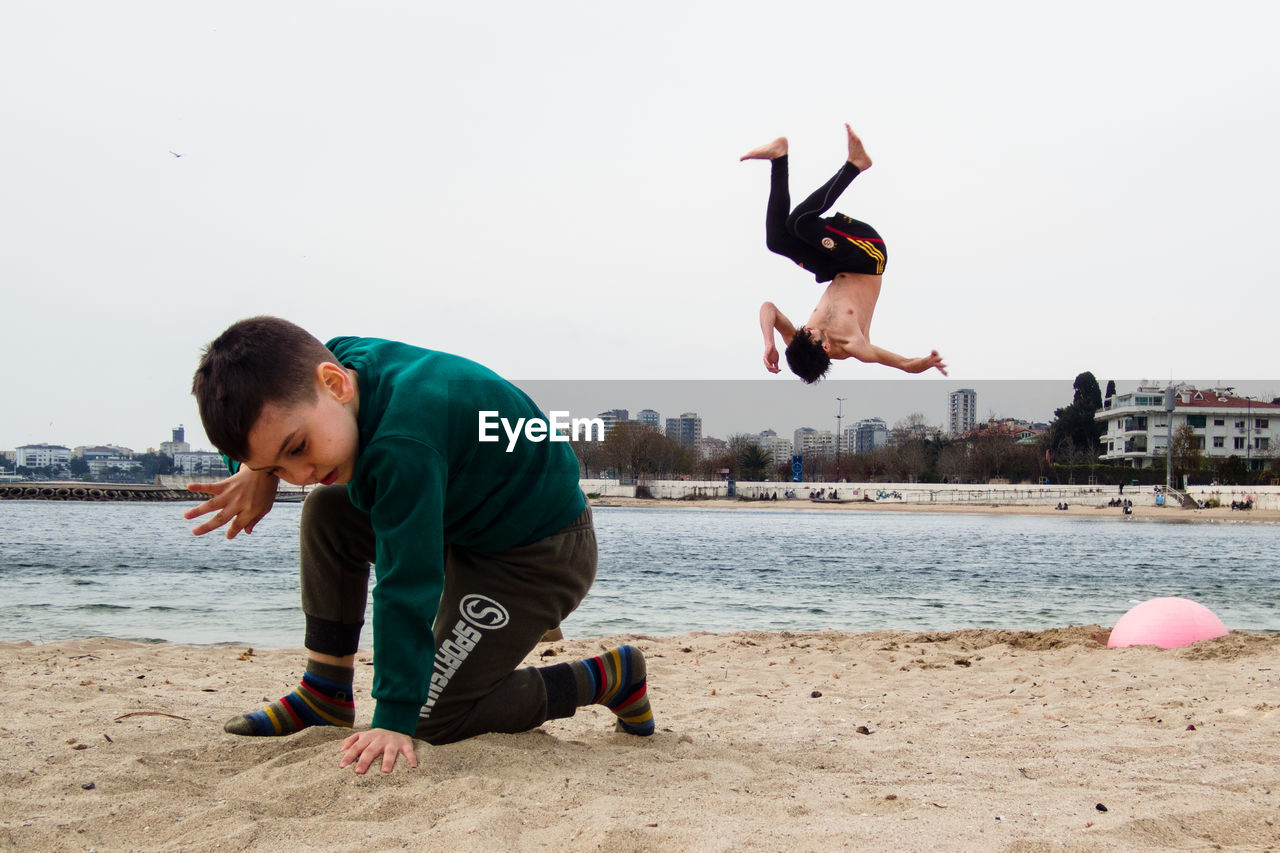 BOY ON BEACH AGAINST SKY