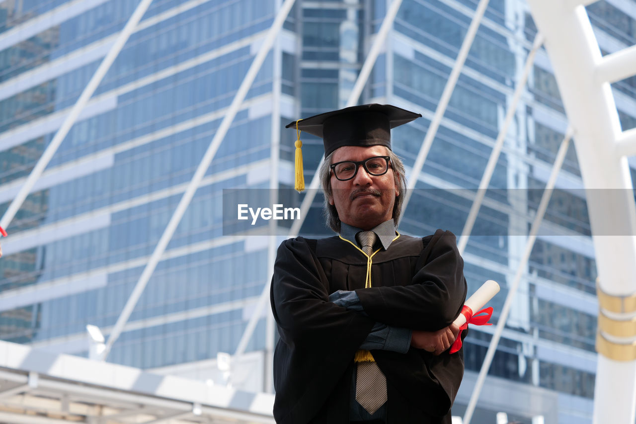 Portrait of businessman in graduation gown against office building