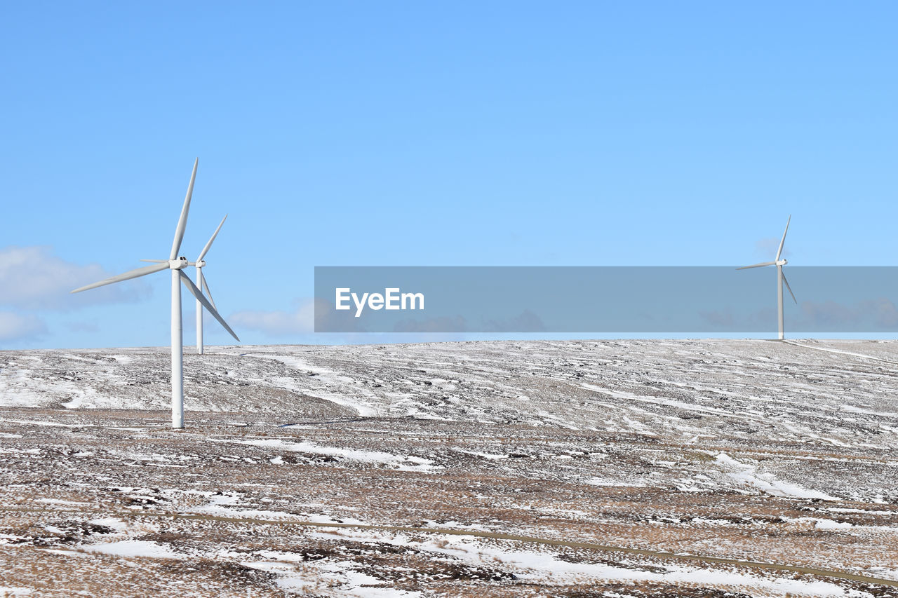 Low angle view of wind turbines against clear blue sky