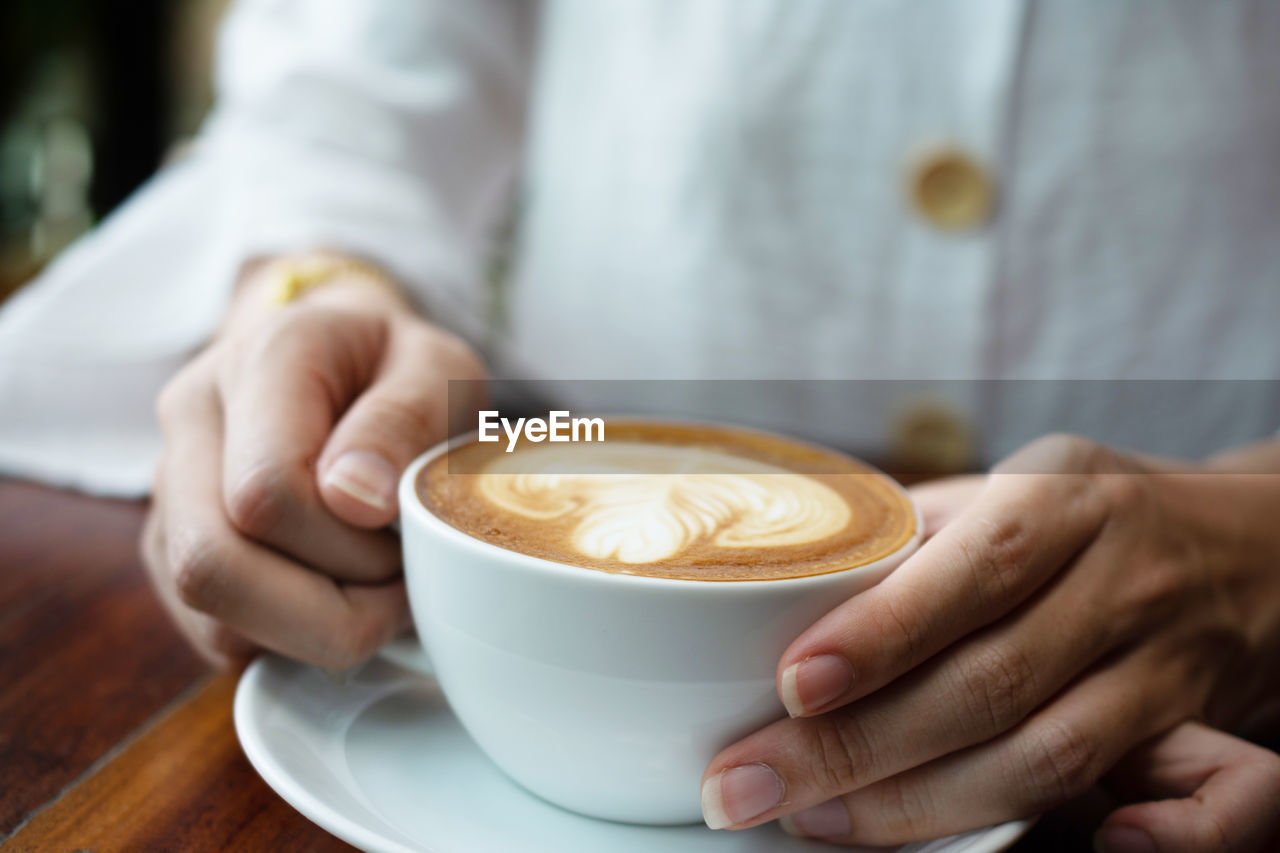 CROPPED IMAGE OF WOMAN HOLDING COFFEE CUP WITH CAPPUCCINO
