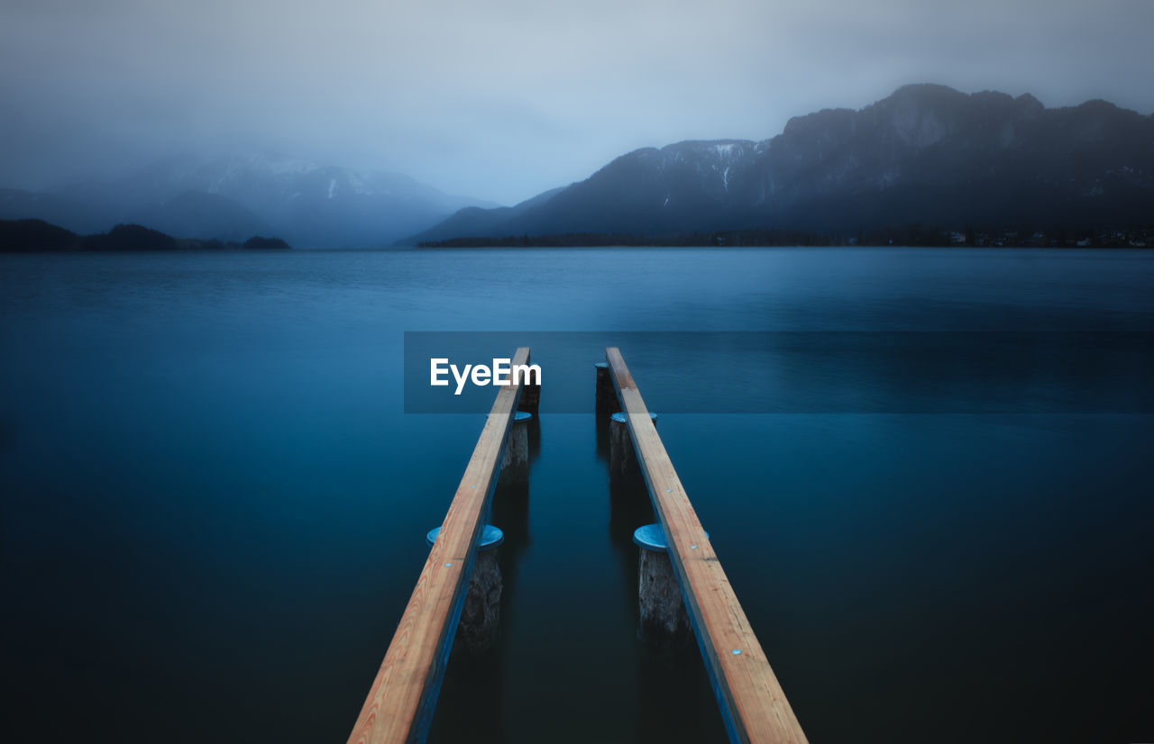 Wooden posts in lake against sky