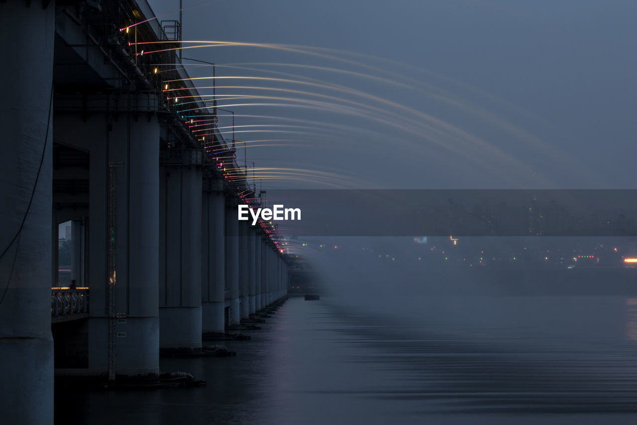 Low angle view of water flowing from bridge in river against sky at dusk