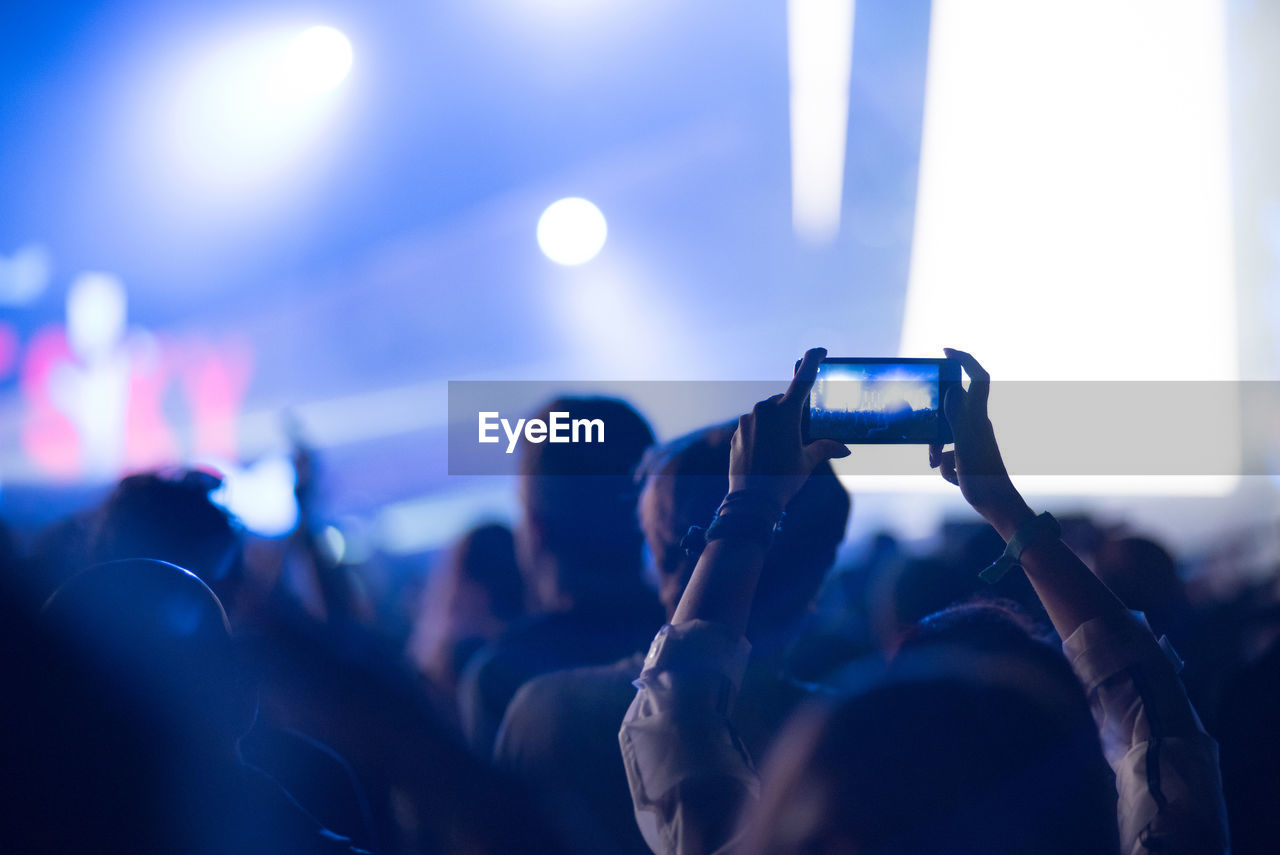 Cropped hands of woman filming over smart phone at music concert