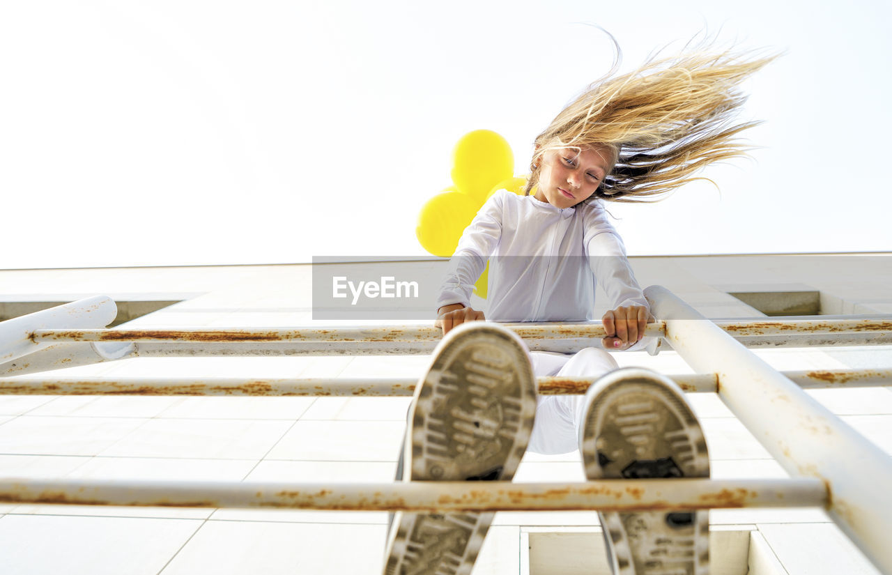 Low angle view of girl standing on railing with tousled hair during sunny day