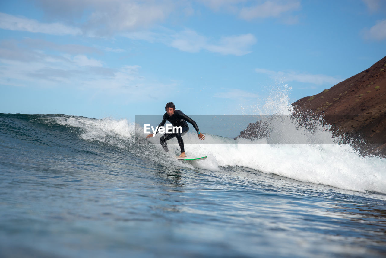 Full length portrait of man surfing in sea against sky