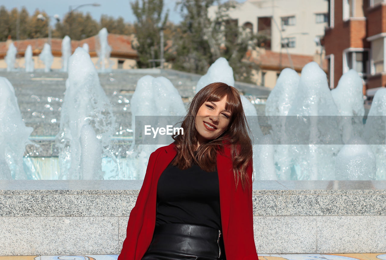 Portrait of smiling young woman sitting against fountain