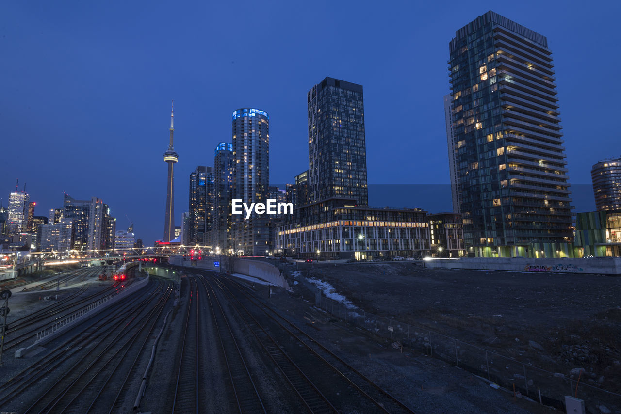 Railroad tracks in illuminated city against clear sky at dusk