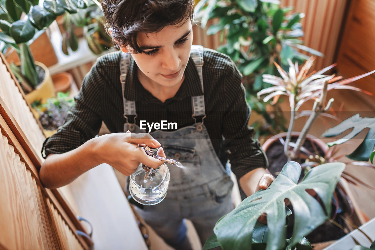 Young girl watering home plants on the balcony, green environment in room, home gardening