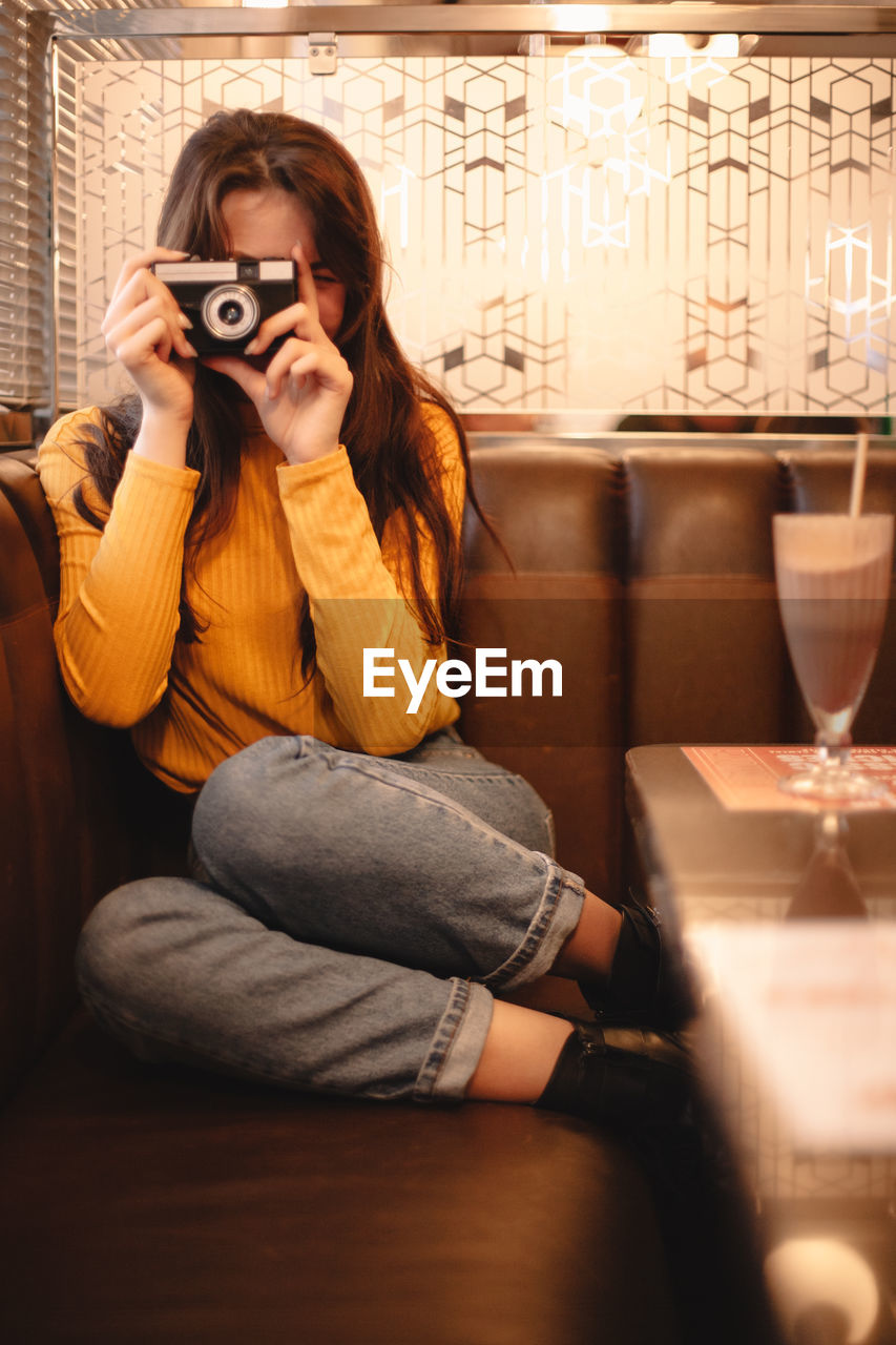 Teenage girl photographing with vintage camera while sitting in cafe