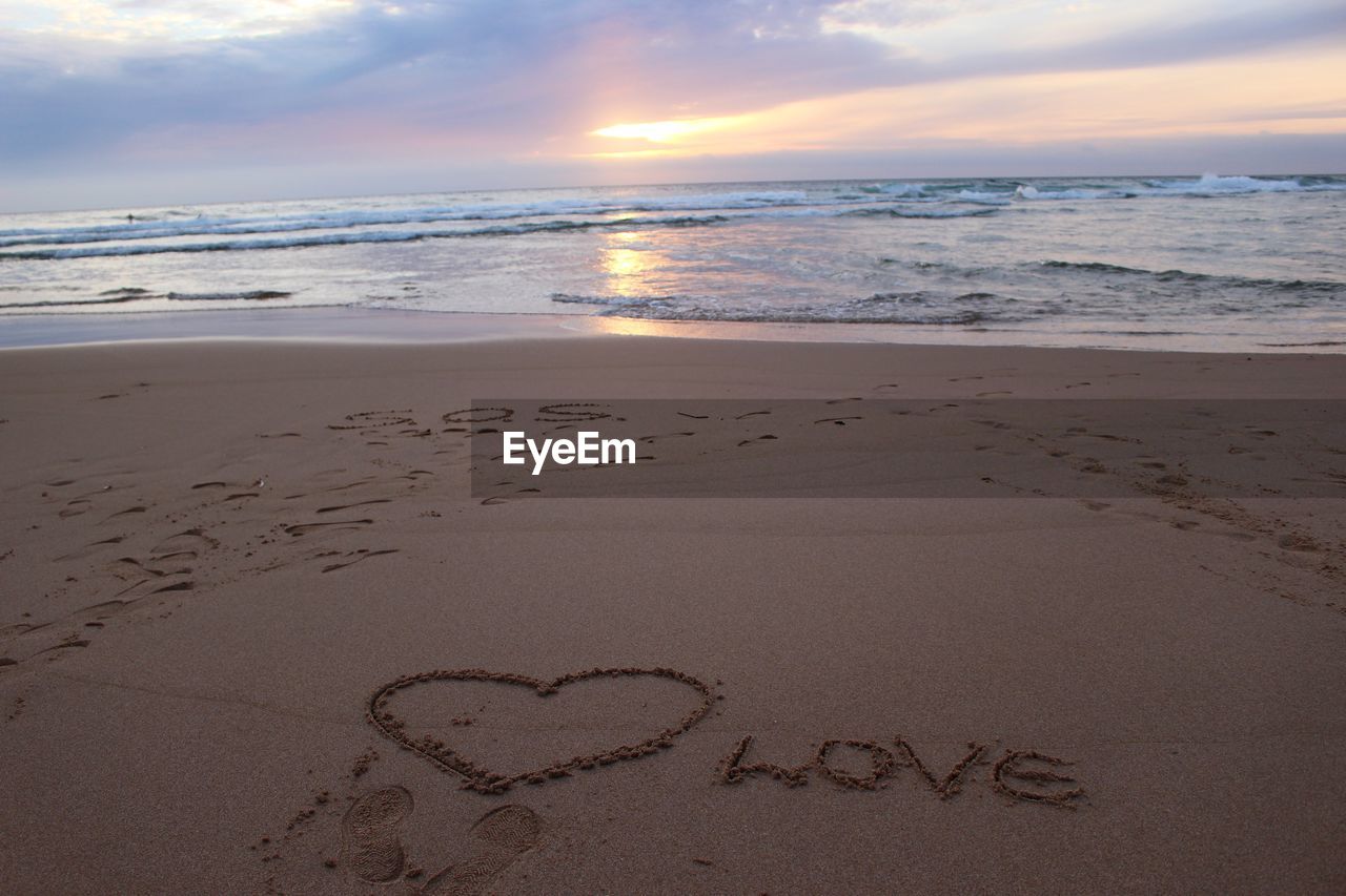 Text on sand at beach against sky during sunset