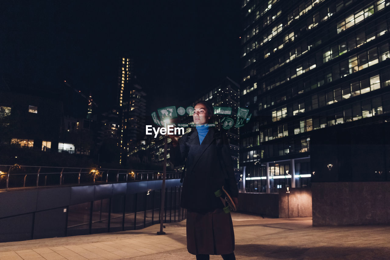 Woman using augmented reality standing on footpath at night