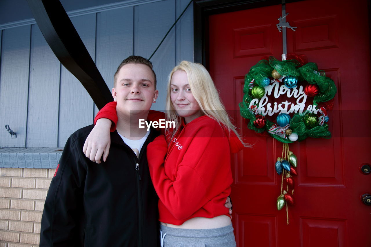 Portrait of smiling young siblings standing against house during christmas