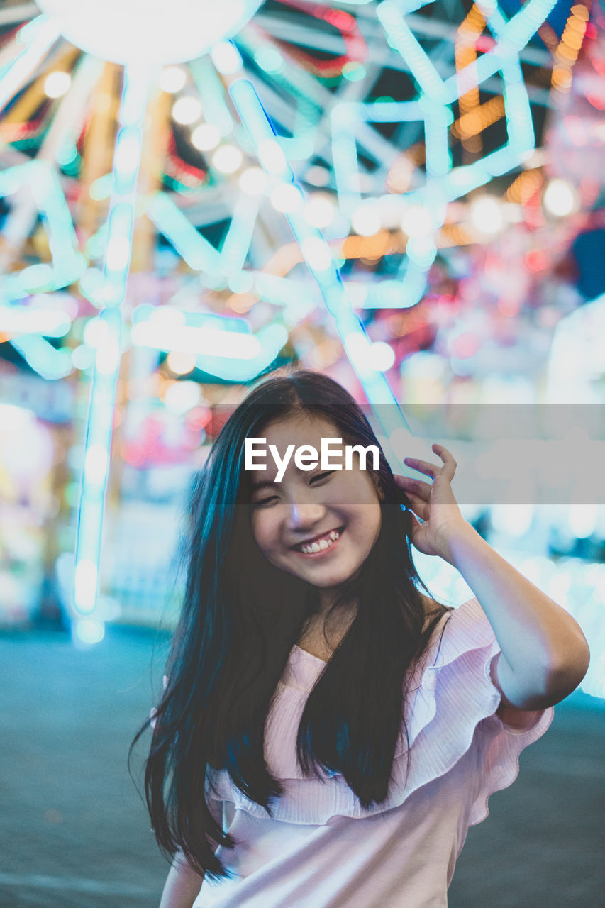 Smiling young woman standing at amusement park during night