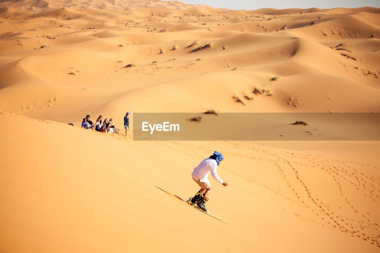 Person sandboarding in desert against clear sky