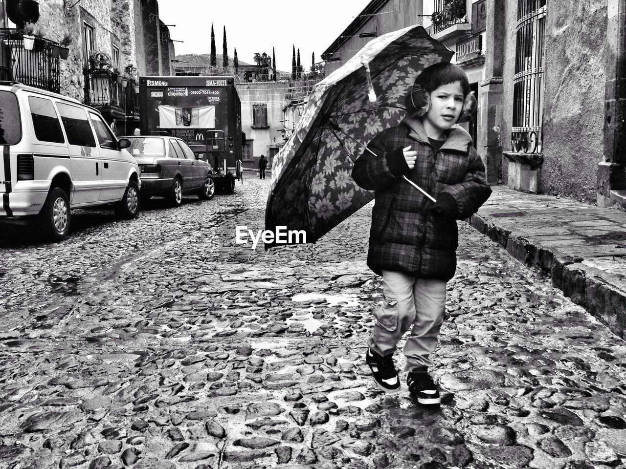 Full length portrait of boy walking on wet street with umbrella