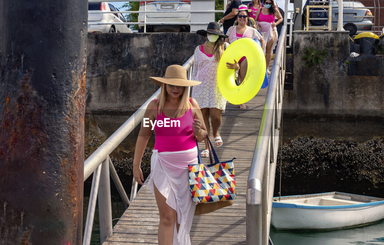 Women in bikinis walking down a walkway to the pier. 