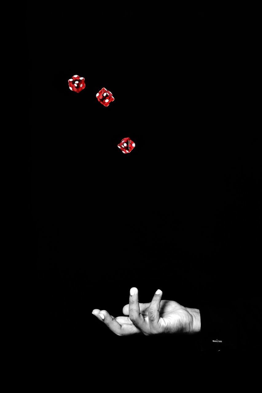 Cropped hand of man with dices in mid-air against black background
