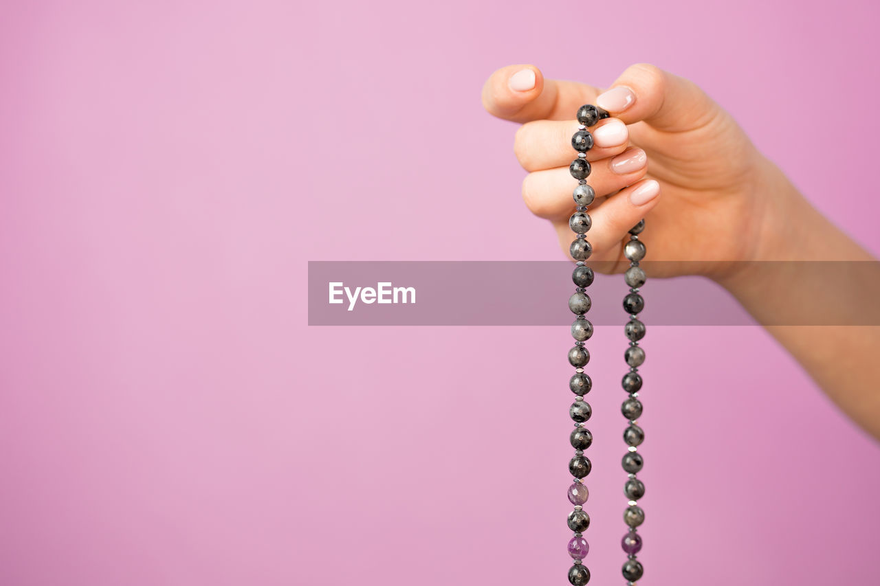 Cropped hand of woman holding bead necklace against colored background