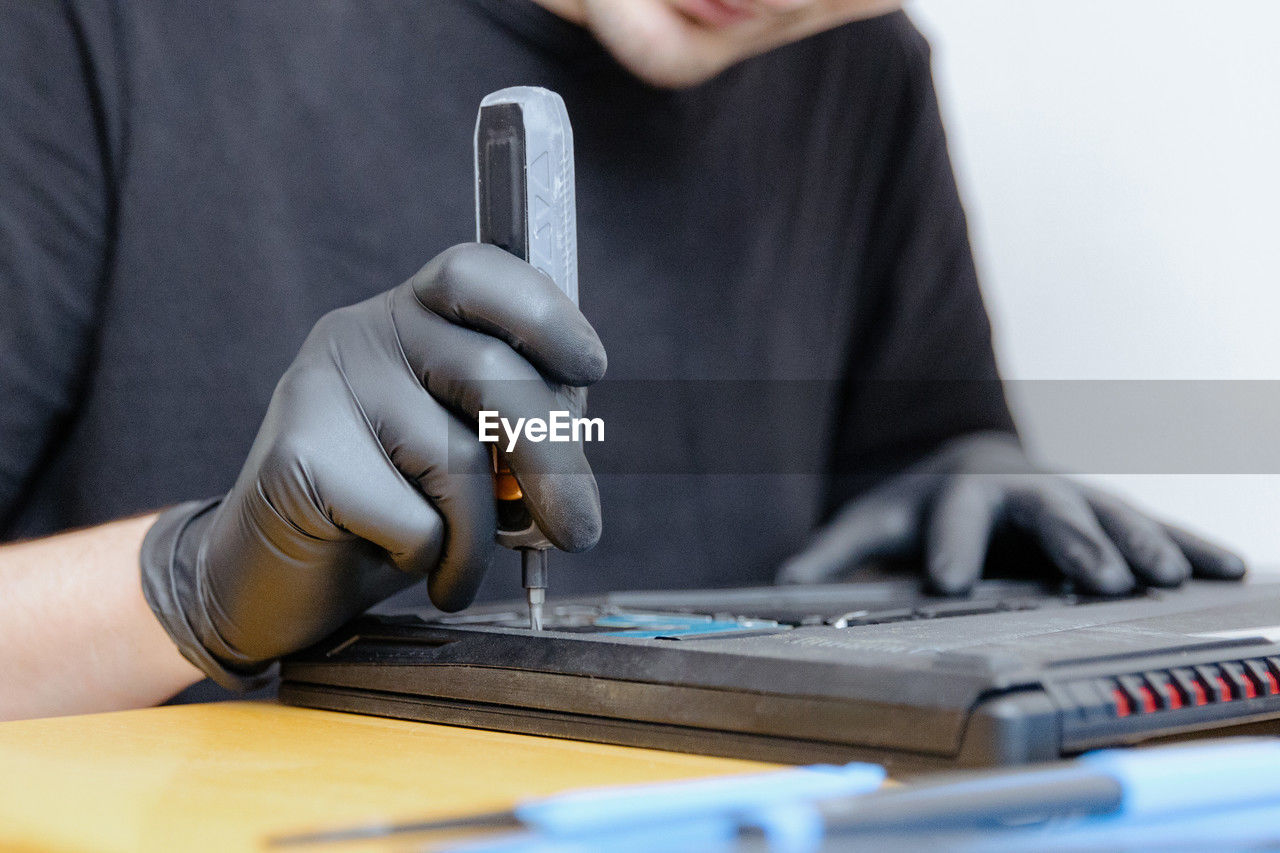 A man unscrews a bolt on a laptop with a screwdriver.