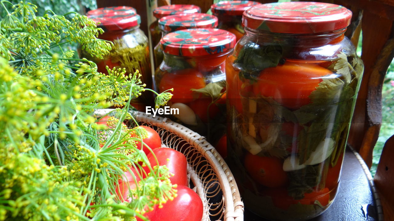 High angle view of tomatoes in bowl by jars and herbs on table