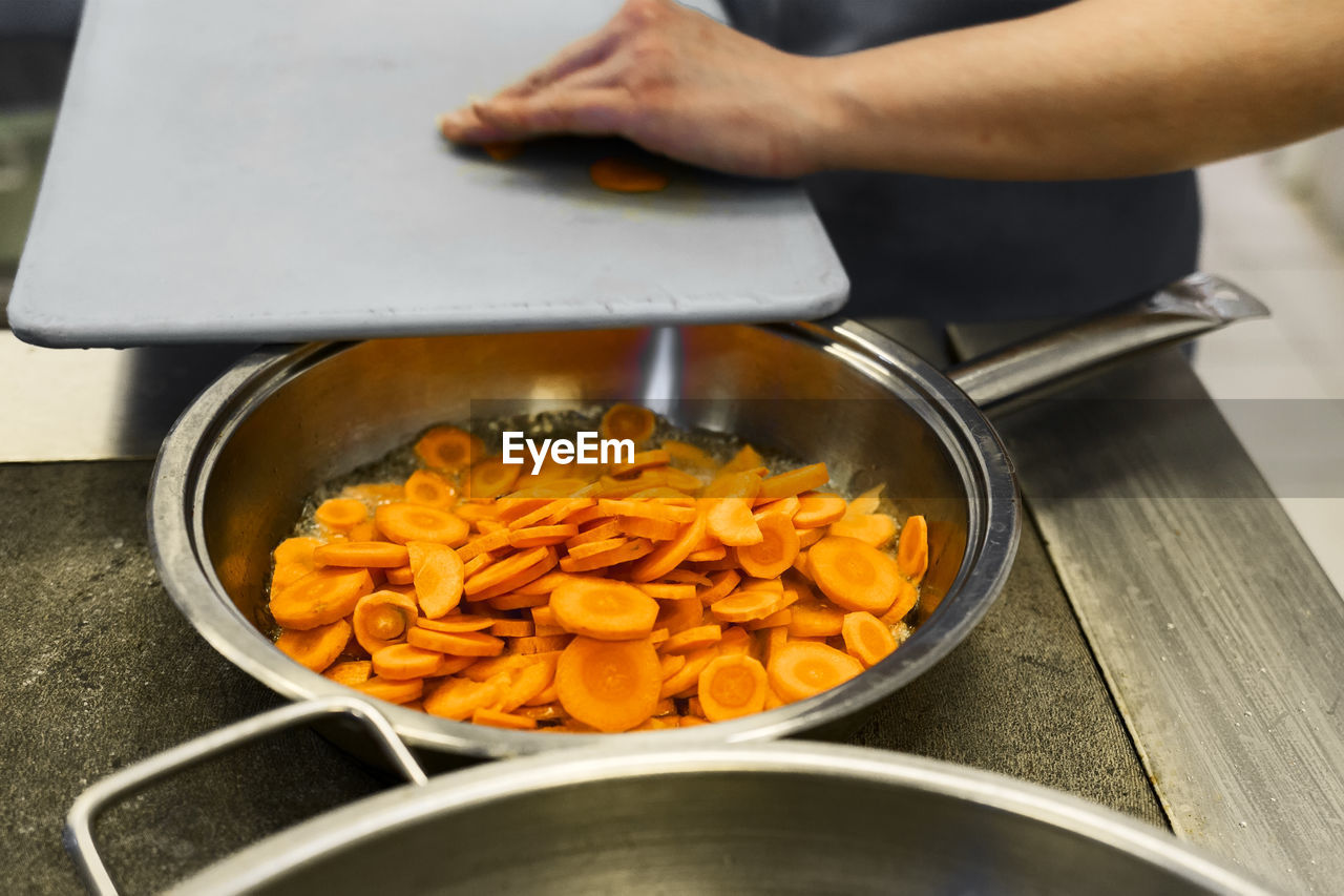 A cook prepares lunch in a fast food cafeteria. fry the carrots in a pan.