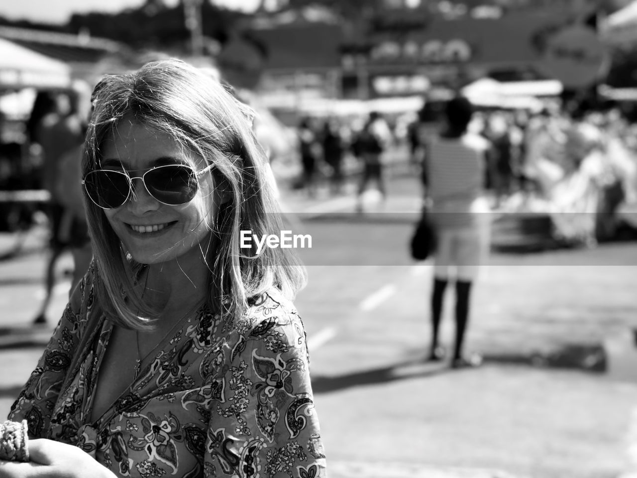 Portrait of young woman standing in city wearing sunglasses smiling while on her mobile phone