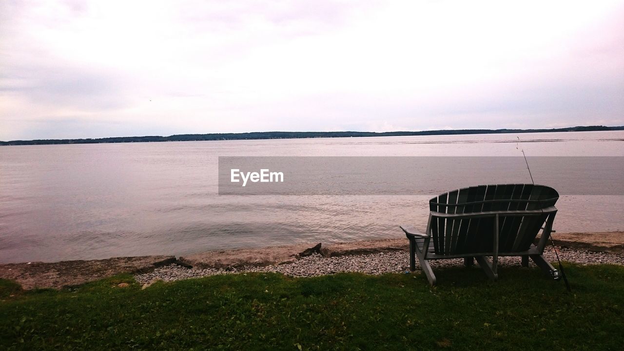 Empty bench by lake against sky