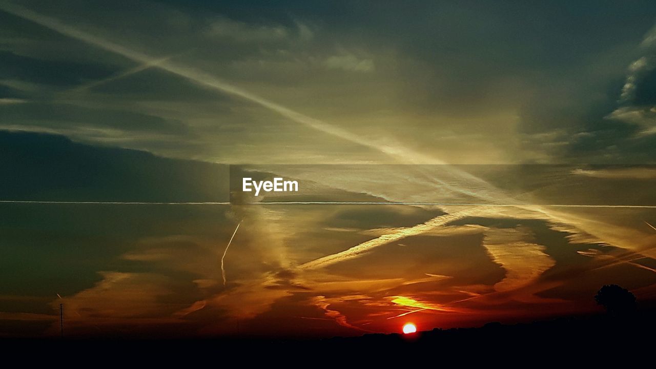 Scenic view of silhouette vapor trails against sky during sunset