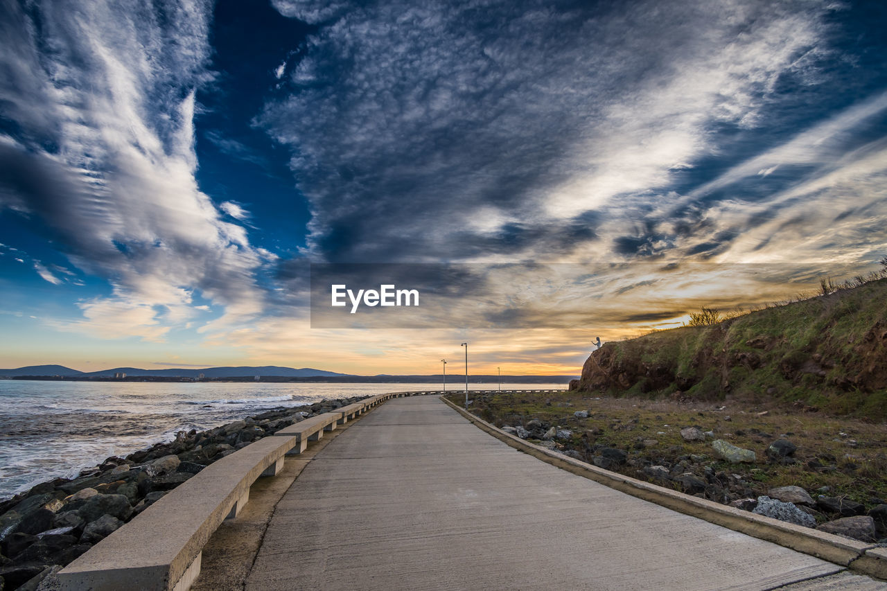 Road by sea against sky during sunset