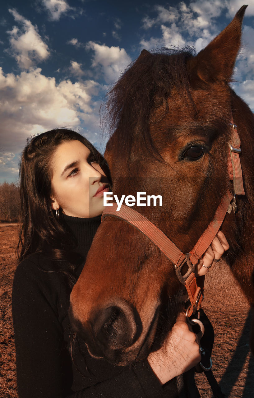 Young woman with horse against cloudy sky