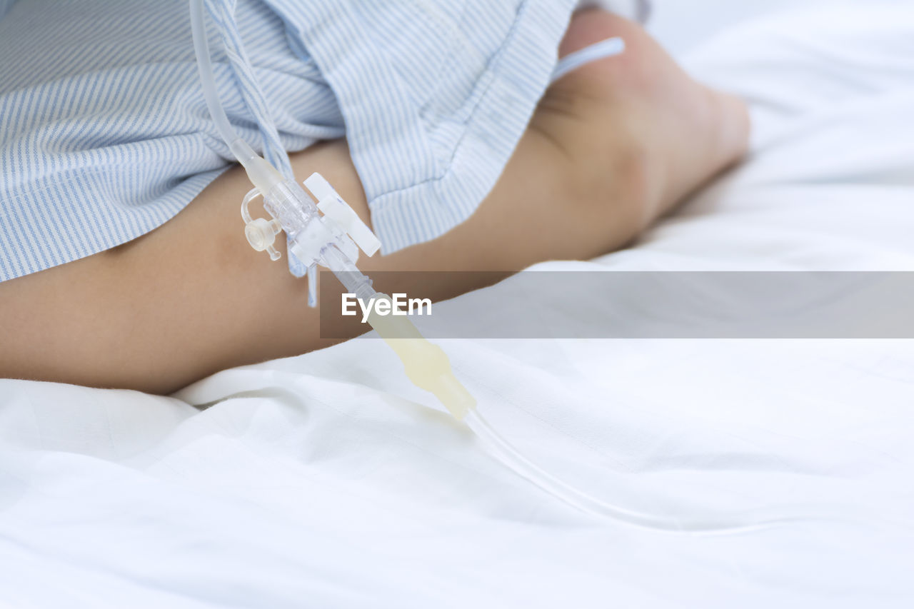 Midsection of person with iv drip relaxing on bed