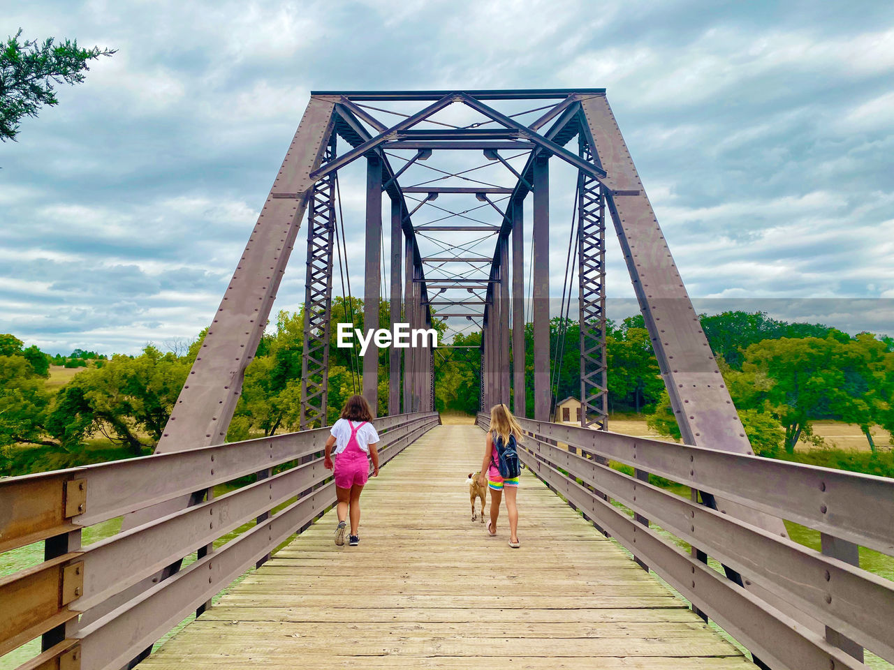 Girls walking on footbridge against cloudy sky