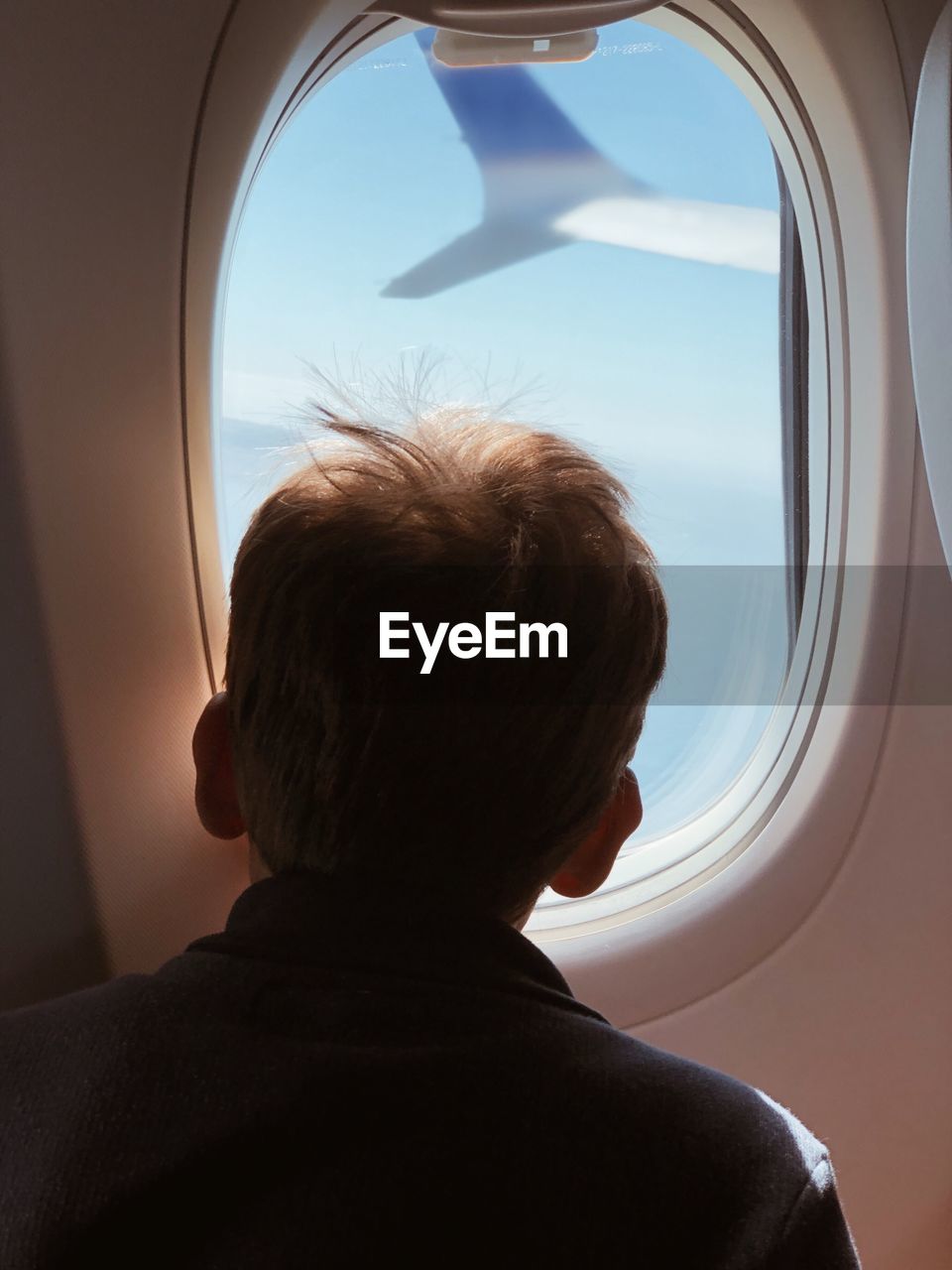Rear view of boy looking through airplane window