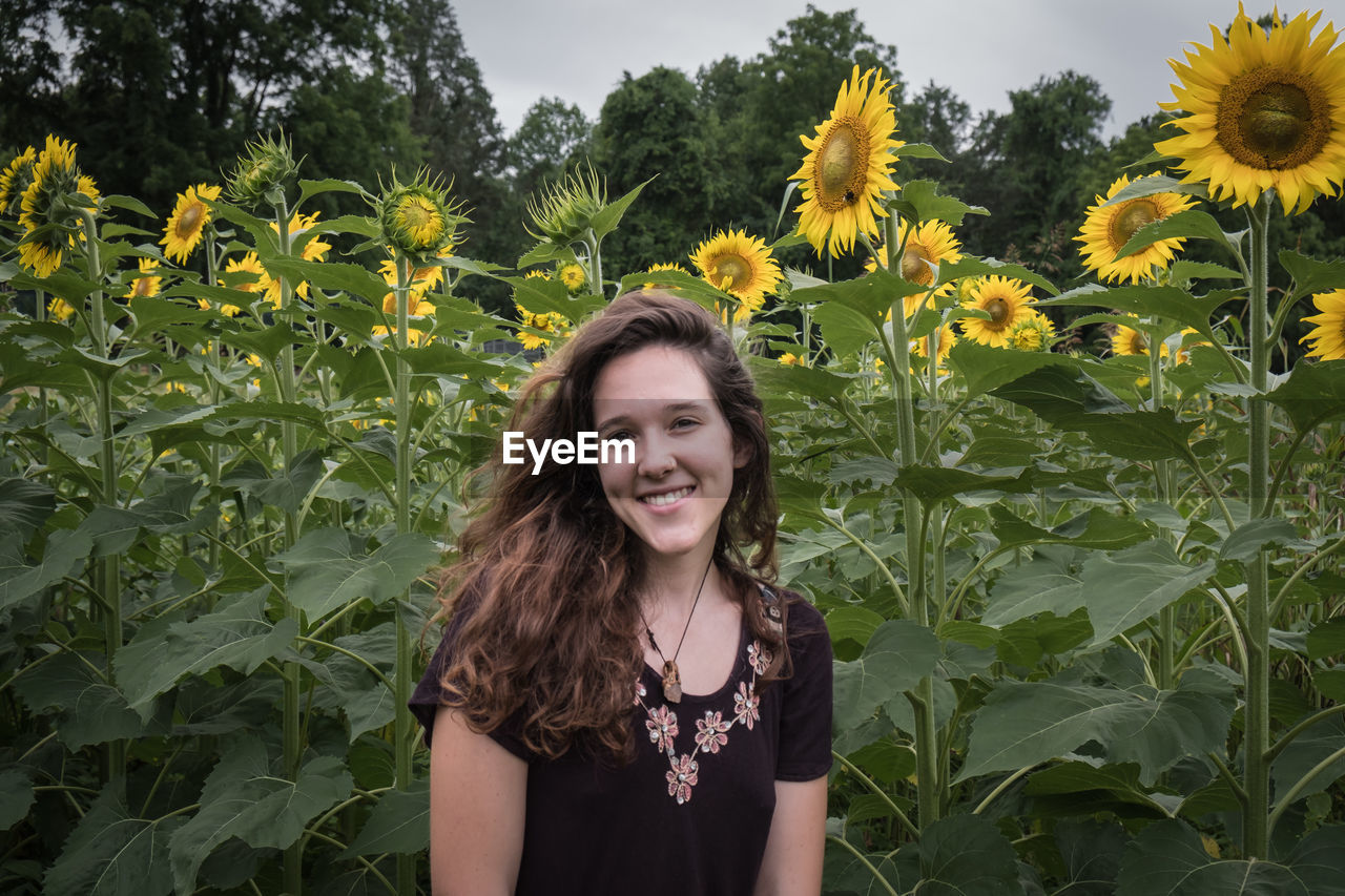 Portrait of smiling beautiful woman against sunflowers at field