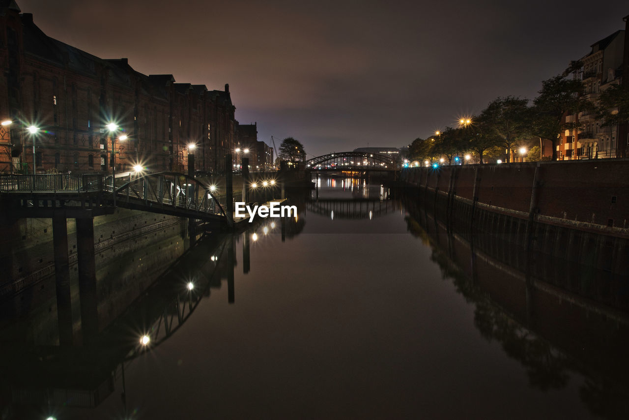 ILLUMINATED BRIDGE OVER RIVER AT NIGHT