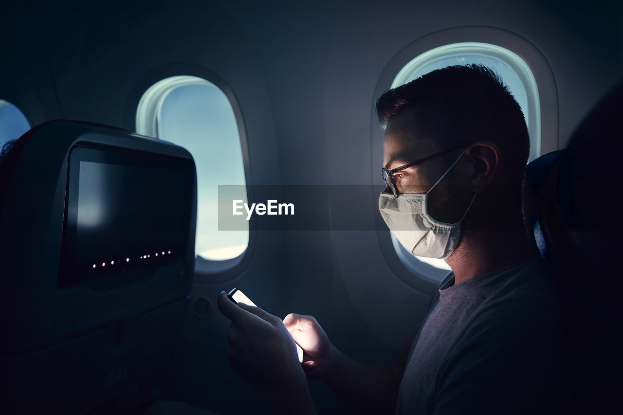 Man with face mask traveling by airplane. passenger using phone during flight.