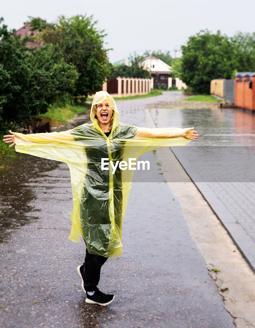 Portrait of woman wearing raincoat standing on road in rainy season