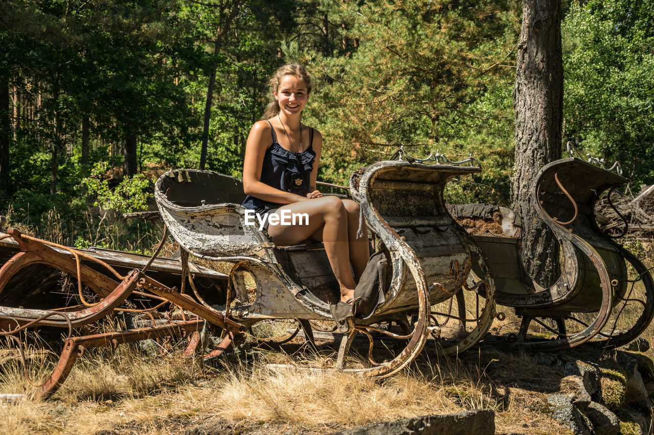 Portrait of smiling young woman sitting on cart against trees