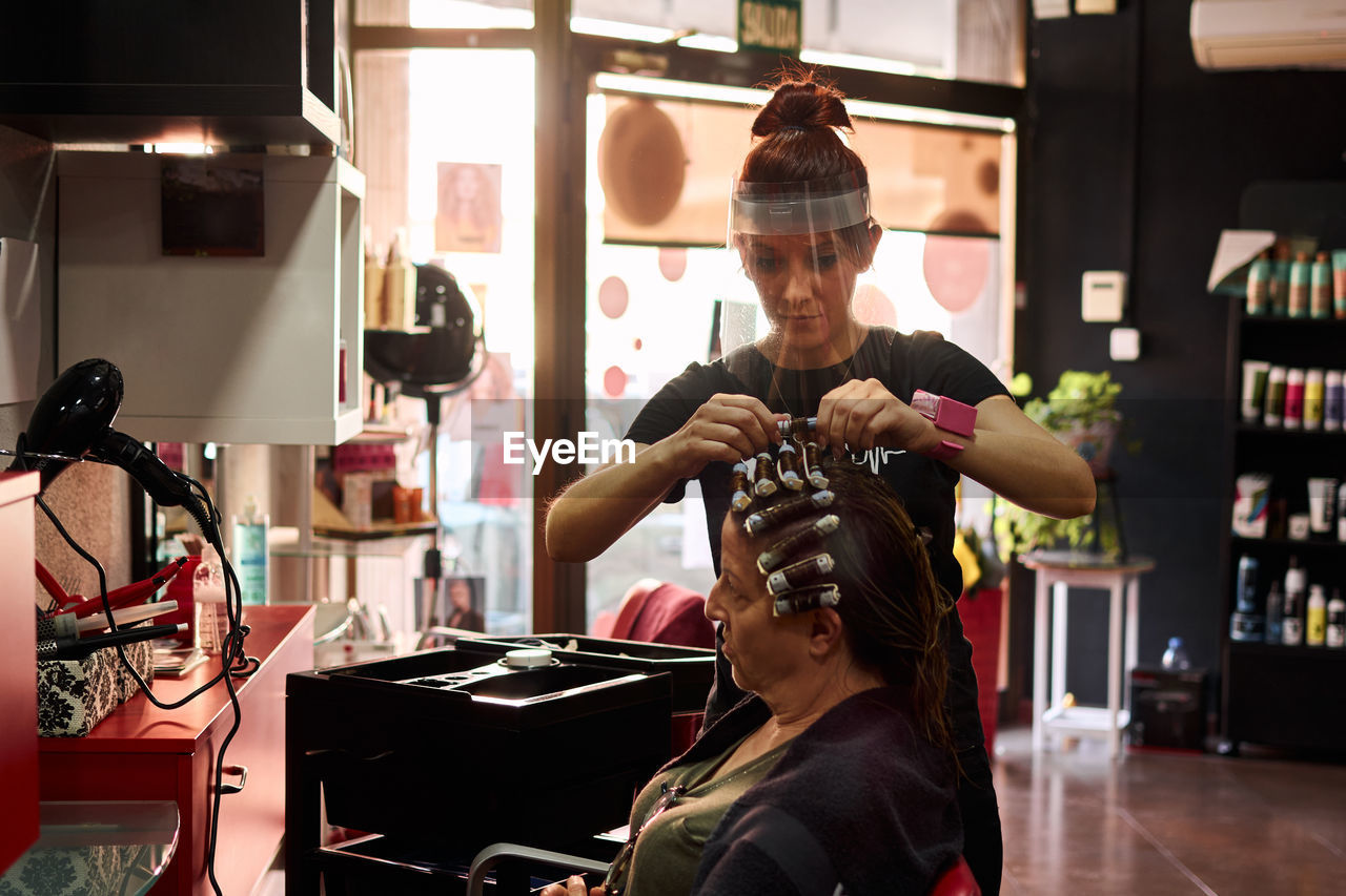 Hairdresser combs a client with a face shield in her salon