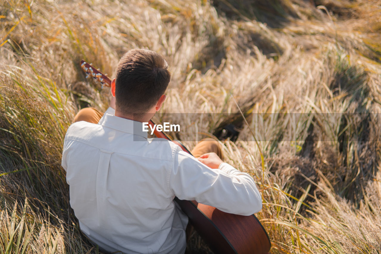 Man with acoustic guitar sits in the autumn grass, tranquil scene