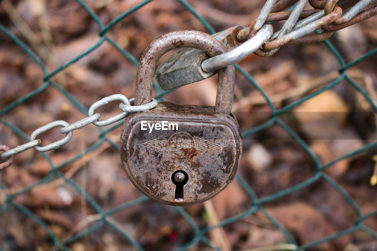 Close-up of rusty chain with padlock on chainlink fence